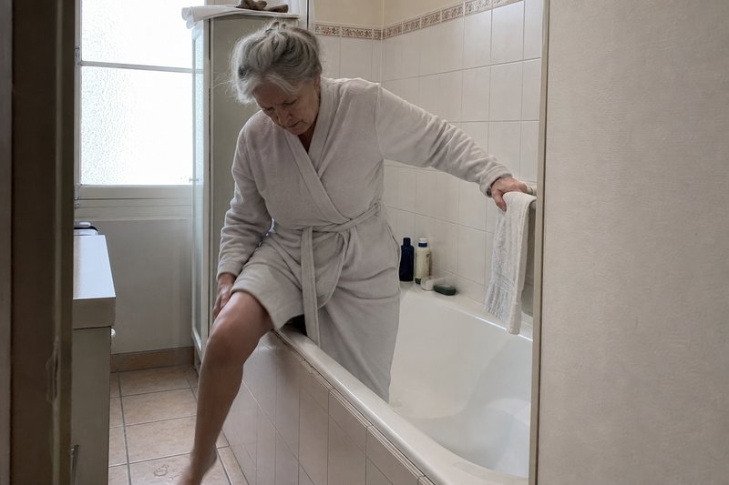 Femme senior s'appuyant au porte-serviettes en sortant de la baignoire