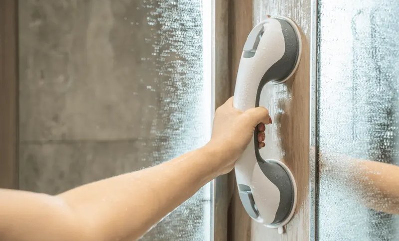 Poignée d'appui posée sur une paroi de douche vitrée, une main en appui