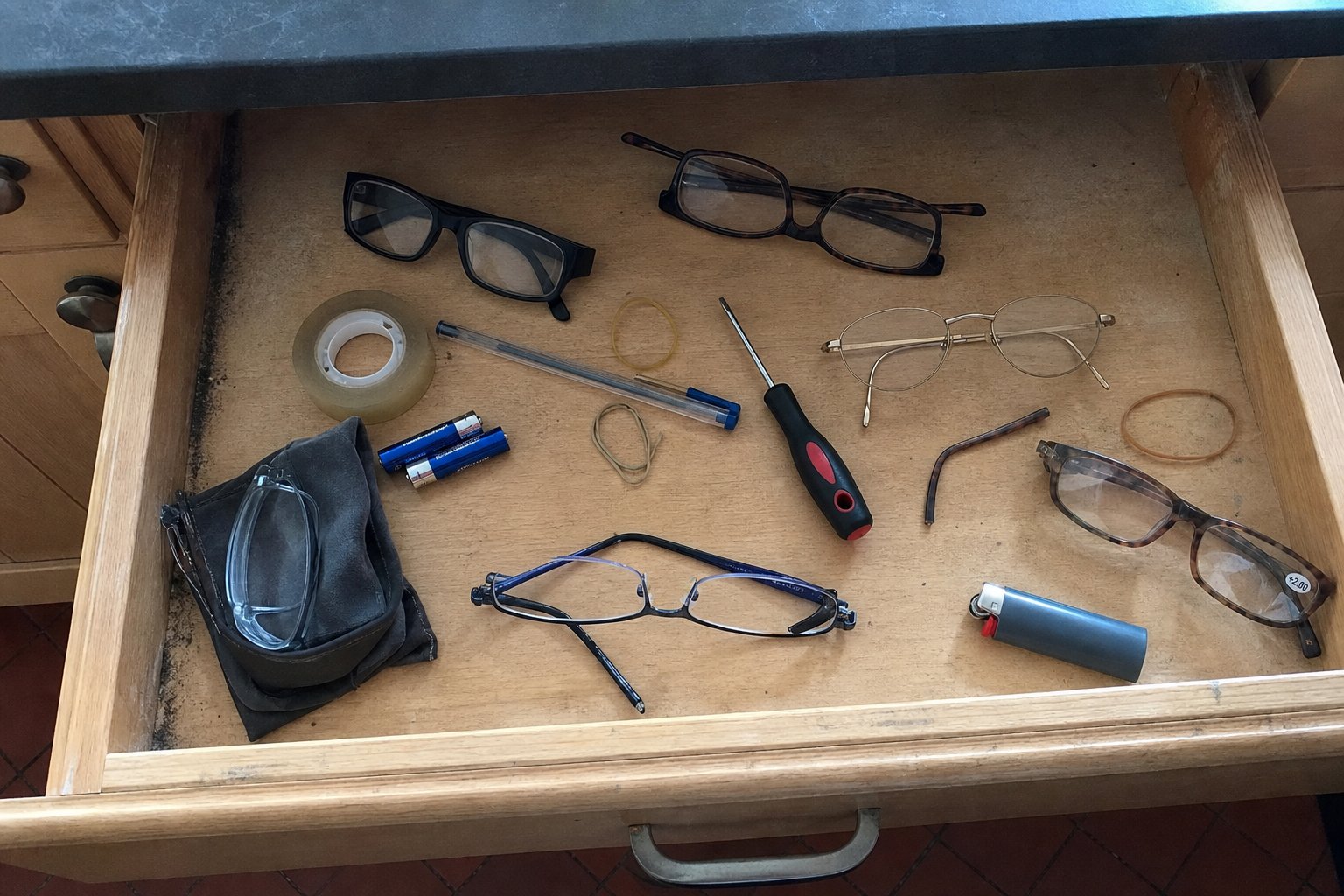 Un tiroir de cuisine ouvert, rempli de plusieurs paires de lunettes de lecture dépareillées