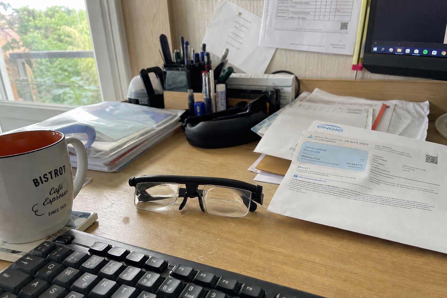 Les lunettes posées sur un bureau à côté d'un clavier, d'une tasse et de courriers