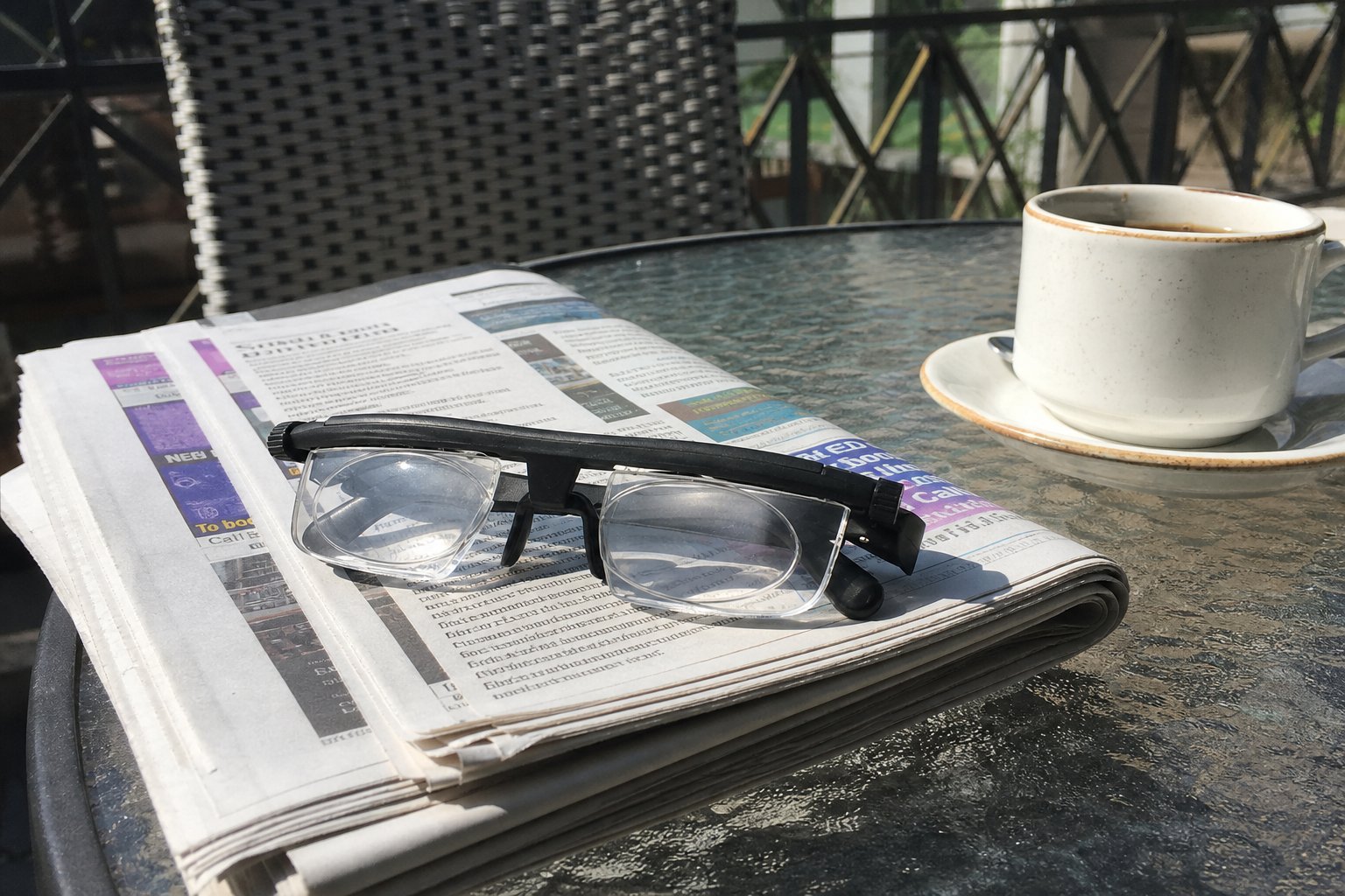 Les lunettes posées sur un journal plié à côté d'une tasse de café, sur une table extérieure