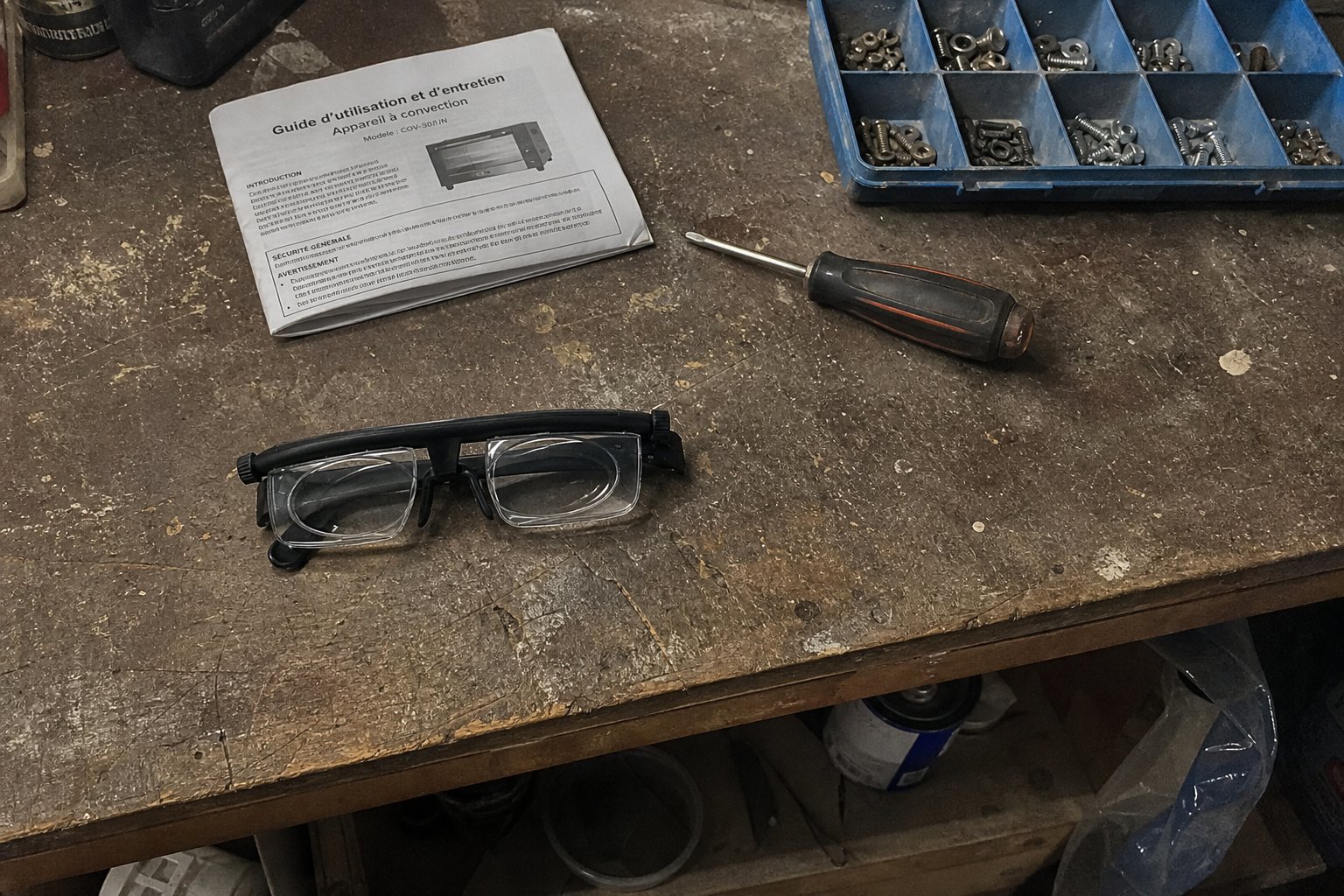 Les lunettes posées sur un établi à côté d'un tournevis, d'un casier à visses et d'une notice